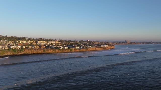 Aerial view of the cliffs, the surf and the ocean at Bird Rock, with surfers out.