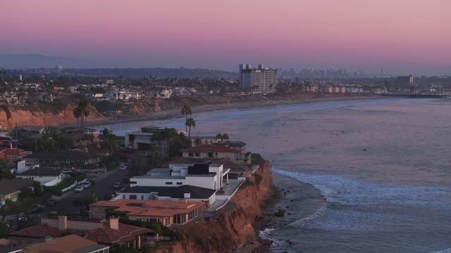 Aerial view of the cliffs, the skyline and palm trees at Bird Rock, with surfers out.