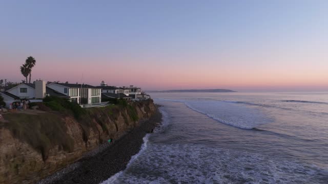 Low aerial view of the cliffs, the surf and palm trees at Bird Rock, with people walking.