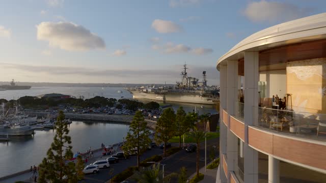 Low aerial view of the harbor, boats and palm trees at Embarcadero, with a crowd gathered.
