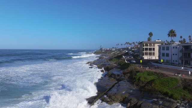Low aerial view of the cliffs, the surf and palm trees at Beach Barber Tract, with people walking.