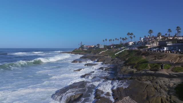 Low aerial view of the cliffs, the surf and palm trees at Beach Barber Tract, with people walking.