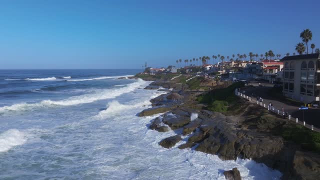 Low aerial view of the cliffs, the surf and palm trees at Beach Barber Tract, with people walking.