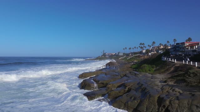 Low aerial view of the cliffs, the surf and palm trees at Beach Barber Tract, with people walking.