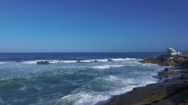 Low aerial view of the cliffs, the surf and the ocean at La Jolla Village.