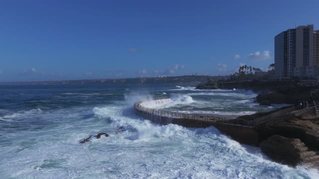 Low aerial view of the cliffs, the surf and the ocean at La Jolla Village.