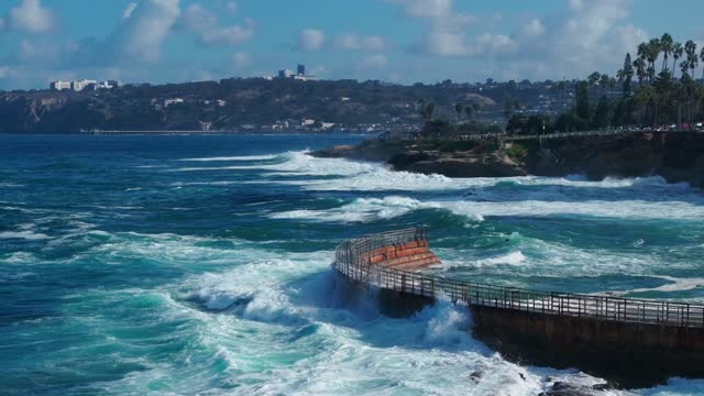 Low aerial view of the cliffs, the surf and palm trees at La Jolla Village.