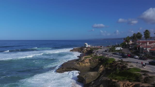 Low aerial view of the cliffs, the surf and palm trees at La Jolla Village, with people walking.