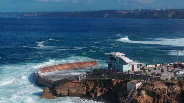 Aerial view of the cliffs, the surf and the pier at La Jolla Village, with people walking.