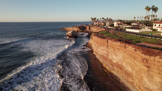 Low aerial view of the cliffs, the surf and palm trees at Sunset Cliffs.