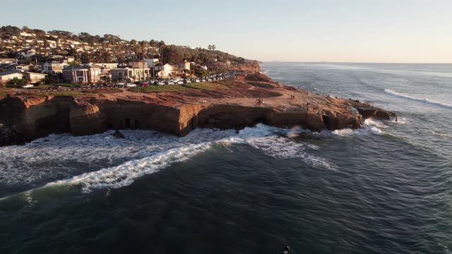 Low aerial view of the cliffs, the surf and the ocean at Sunset Cliffs, with people walking.