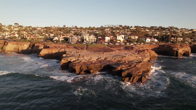 Low aerial view of the cliffs, the surf and palm trees at Sunset Cliffs, with people walking.