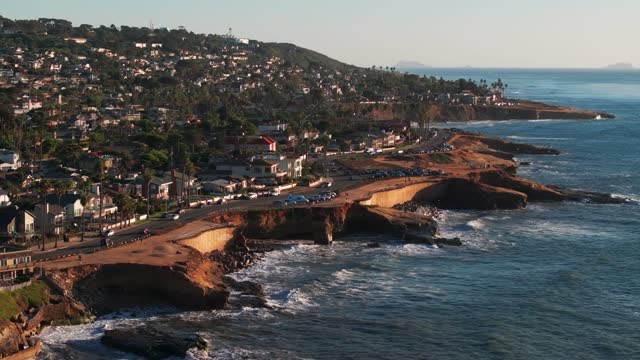 Low aerial view of the cliffs, the surf and palm trees at Sunset Cliffs.