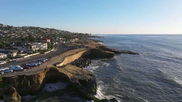 Low aerial view of the cliffs, the ocean and homes at Sunset Cliffs, with people walking.