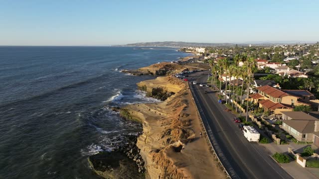 Low aerial view of the cliffs, the surf and palm trees at Sunset Cliffs, with people walking.