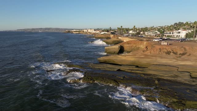 Low aerial view of the cliffs, the surf and palm trees at Sunset Cliffs.