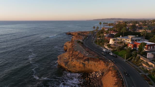 Low aerial view of the cliffs, the surf and palm trees at Sunset Cliffs, with people walking.