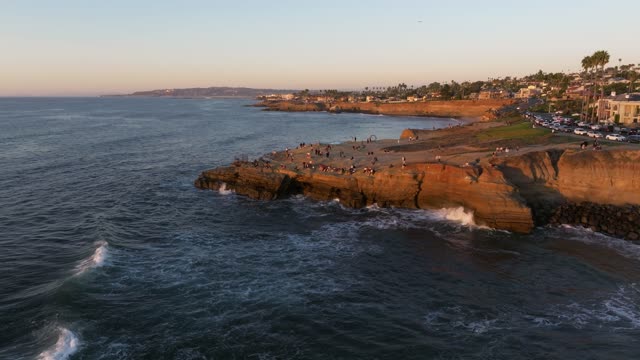 Low aerial view of the cliffs, the surf and palm trees at Sunset Cliffs, with a crowd gathered.