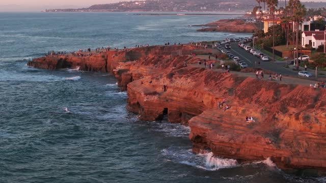 Low aerial view of the cliffs, palm trees and the ocean at Sunset Cliffs, with people walking.