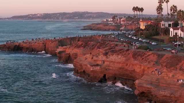 Low aerial view of the cliffs, palm trees and the ocean at Sunset Cliffs, with a crowd gathered.
