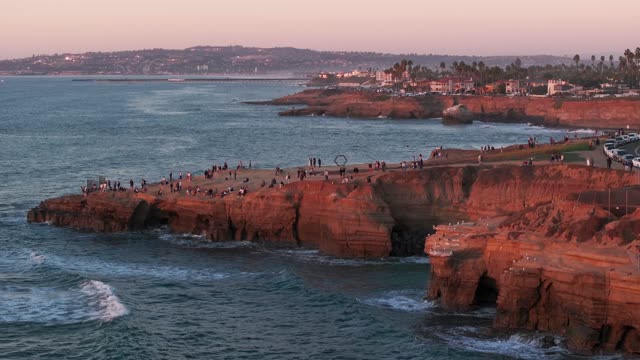 Low aerial view of the cliffs, palm trees and the ocean at Sunset Cliffs, with a crowd gathered.