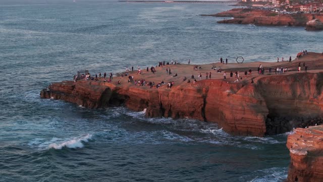 Aerial view of the cliffs, the surf and the ocean at Sunset Cliffs, with a crowd gathered.