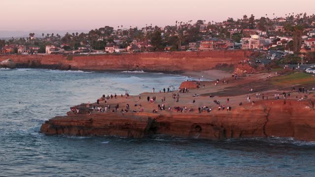 Low aerial view of the cliffs, the surf and palm trees at Sunset Cliffs, with a crowd gathered.