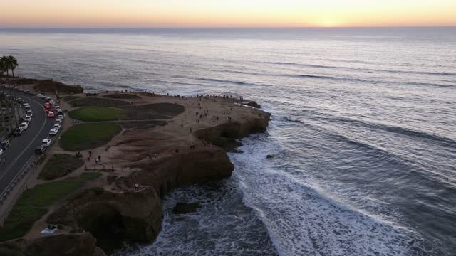 Aerial view of the cliffs, the surf and the ocean at Sunset Cliffs, with a crowd gathered.