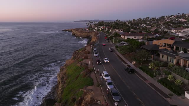 Low aerial view of the cliffs, the surf and palm trees at Sunset Cliffs, with people walking.