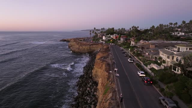 Low aerial view of the cliffs, palm trees and the ocean at Sunset Cliffs, with people walking.