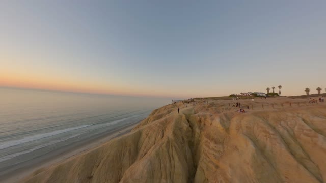 Low aerial view of the cliffs, palm trees and the ocean at Black’s Beach, with people walking.