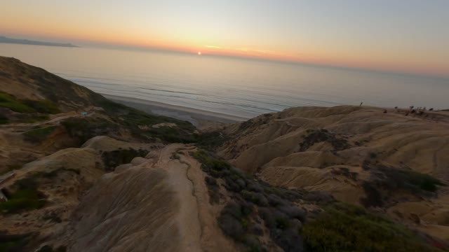 Low aerial view of the cliffs, the ocean and the beach at Black’s Beach, with people walking.