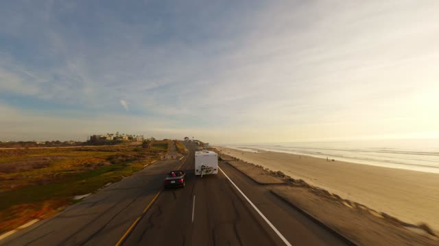 Low aerial view of the beach, the ocean and traffic in Carlsbad, with people walking.