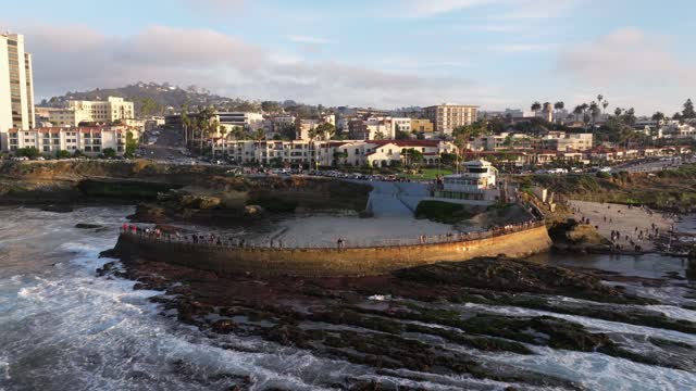 Low aerial view of the beach, the surf and palm trees at La Jolla Cove, with people walking.