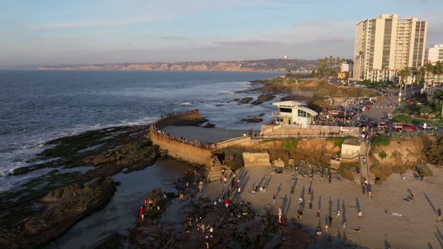 Low aerial view of the beach, the surf and the ocean at La Jolla Cove, with a crowd gathered.