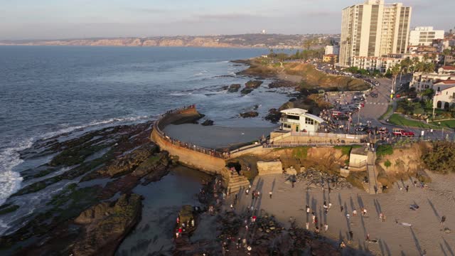 Aerial view of the cliffs, the ocean and the buildings at La Jolla Cove, with a crowd gathered.
