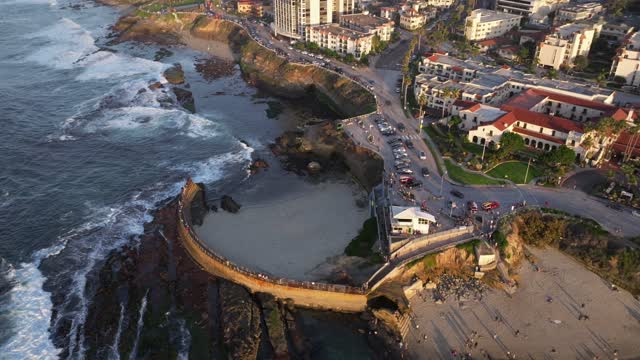Aerial view of the cliffs, the surf and the ocean at La Jolla Cove, with people walking.