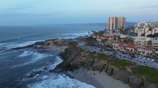 Aerial view of the cliffs, the surf and palm trees at La Jolla Cove, with people walking.