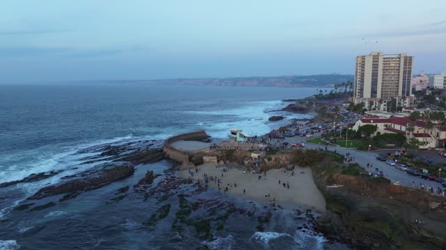 Aerial view of the cliffs, the ocean and homes at La Jolla Cove, with a crowd gathered.
