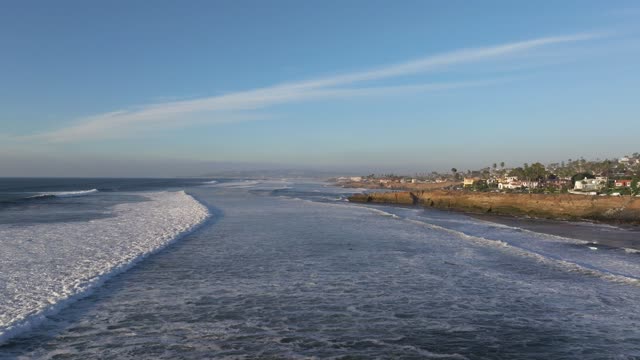Low aerial view of the cliffs, the surf and palm trees at Sunset Cliffs.