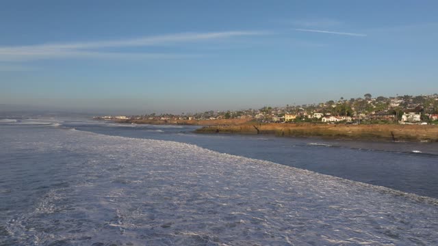 Low aerial view of the cliffs, the surf and palm trees at Sunset Cliffs.