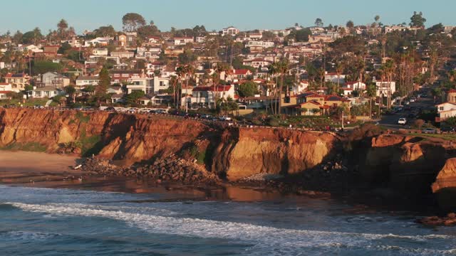 Low aerial view of the cliffs, the surf and palm trees at Sunset Cliffs.