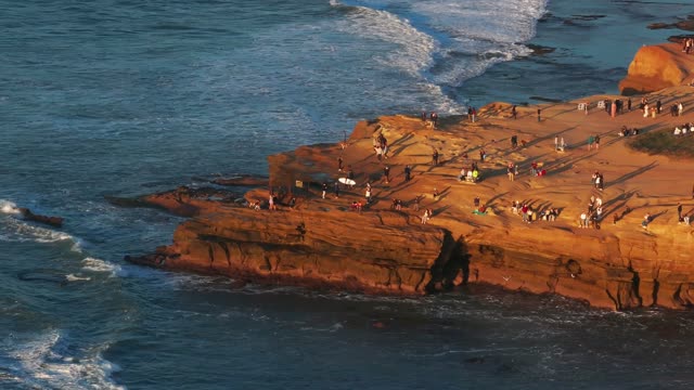 Aerial view of the cliffs, the surf and the ocean at Sunset Cliffs, with a crowd gathered.