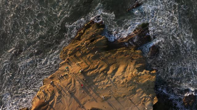 Aerial view of the cliffs, the surf and the ocean at Sunset Cliffs, with people walking.