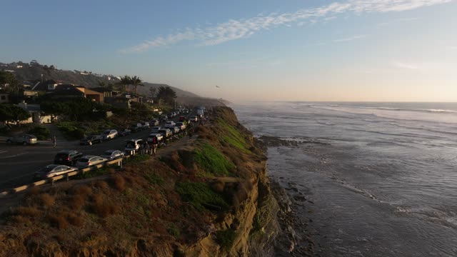Low aerial view of the cliffs, the surf and palm trees at Sunset Cliffs, with people walking.