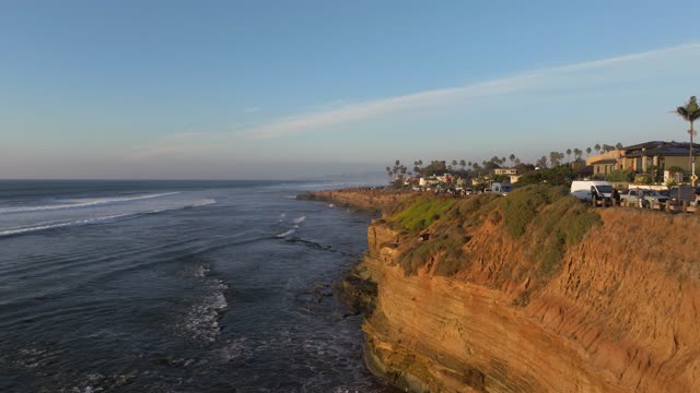 Low aerial view of the cliffs, the surf and palm trees at Sunset Cliffs.