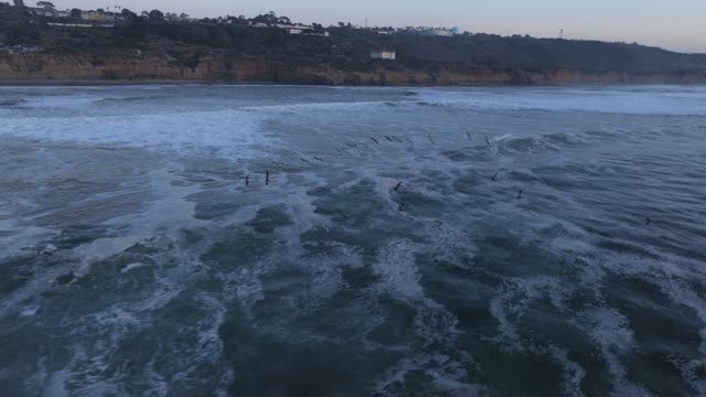 Low aerial view of the cliffs, the surf and the ocean at Sunset Cliffs, with surfers out.