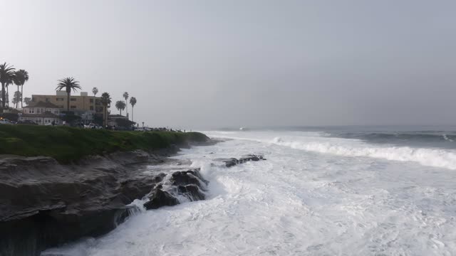The cliffs, the surf and palm trees at La Jolla Cove, with people walking.
