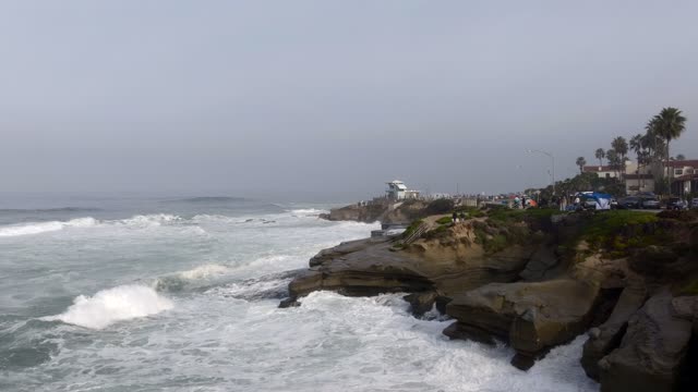 The cliffs, the surf and palm trees at La Jolla Cove, with people walking.