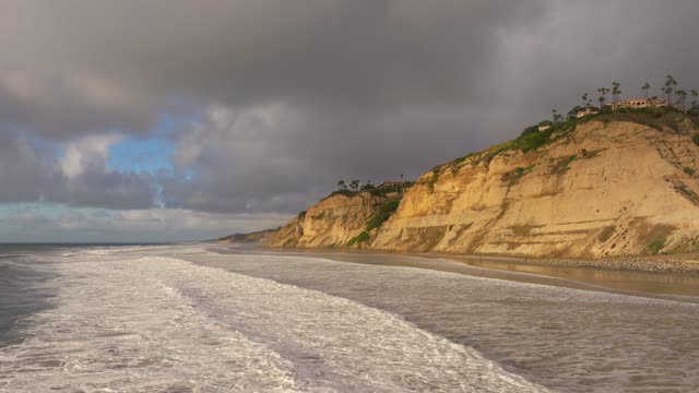 Low aerial view of the cliffs, the surf and palm trees at Black’s Beach.